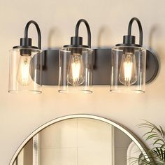 three light bathroom fixture with clear glass shades and black metal frame, on a white wall