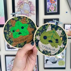 someone holding up two hand embroidered hoop art pieces