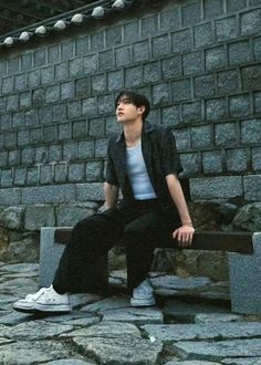 a young man sitting on top of a stone bench next to a brick wall with his eyes closed