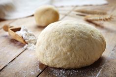 a ball of bread sitting on top of a wooden table next to a scoop of flour