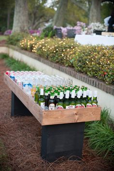 bottles of beer are lined up on a wooden bench in the middle of a garden