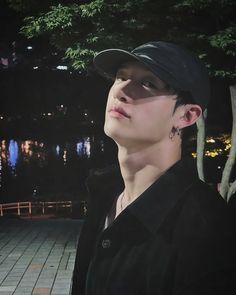 a young man wearing a black hat standing in front of a tree at night with his eyes closed