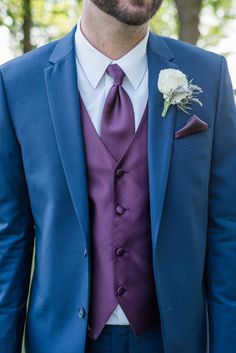 a man in a blue suit with a purple tie and white rose boutonniere