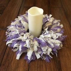 a white candle sitting on top of a wooden floor next to a purple and white wreath