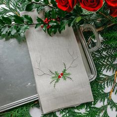 red roses and greenery are on the table next to a silver tray with a napkin