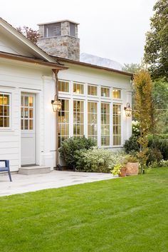 a white house with large windows and green grass in front of the door is a blue bench