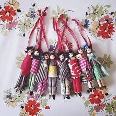 several dolls are hanging from red ribbon on a floral wallpapered background with flowers