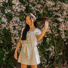 a woman standing in front of a bush with flowers on it and wearing a white dress