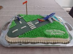 a birthday cake that is shaped like an airport runway and has green grass on it