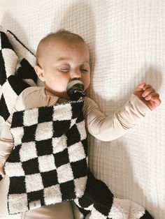 a baby laying on top of a bed next to a black and white checkered blanket