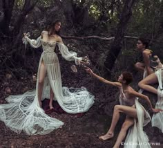 four women in white dresses are sitting on the ground and one woman is holding her hand out