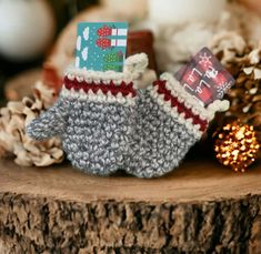 two knitted mittens sitting on top of a piece of wood next to pine cones