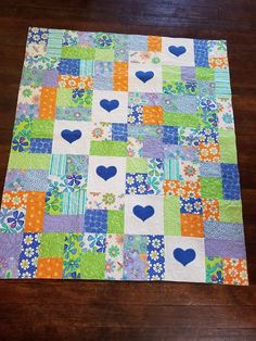 a patchwork quilt on a wooden floor with blue hearts in the center and green, purple, orange, and white squares