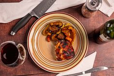 a plate with some meat and vegetables on it next to two wine glasses, a knife and fork