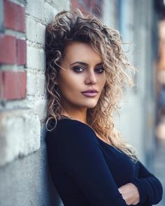 a woman with curly hair leaning against a brick wall