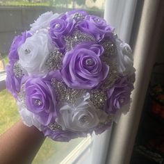 a bride's bouquet with purple and white flowers in front of a window sill