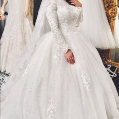 a woman in a white wedding dress standing next to a mirror with dresses on it