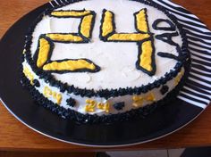 a birthday cake with yellow and black frosting on a wooden table next to a knife