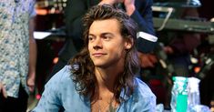 a man with long hair sitting at a table in front of other people and looking off to the side