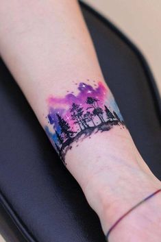 a person's arm with a watercolor painting on it and trees in the background