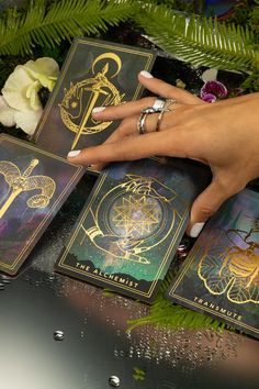 a woman's hand on top of four tarot cards next to some flowers