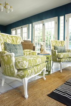 a living room with blue walls and green chairs in it, along with a rug on the floor