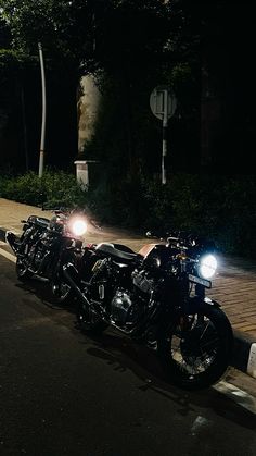 three motorcycles are parked on the side of the road at night with their lights on