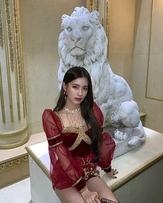 a woman in a red dress sitting on a bench next to a white lion statue