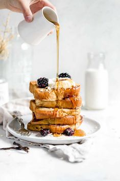 a person pouring syrup onto a stack of waffles on a white plate with berries