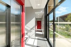 an empty hallway with red door and glass doors leading to another room on the other side