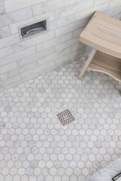 a bathroom with white hexagonal tiles and a wooden bench on the floor next to it