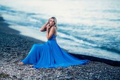 a woman in a blue dress is sitting on the beach talking on her cell phone