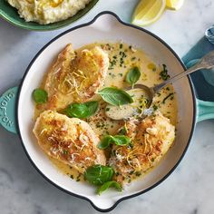 two bowls filled with food on top of a white marble counter next to lemon wedges