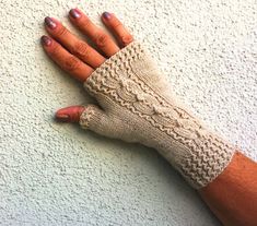 a woman's hand wearing a pair of knitted fingerless gloves on top of a white wall