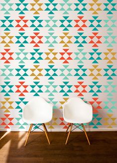 two white chairs sitting in front of a wall with colorful geometric designs on the walls