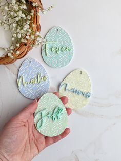 hand holding three decorated cookies with the word hello written on them in blue, green and white