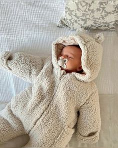 a baby wrapped in a teddy bear outfit sleeping on a bed