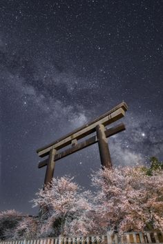 the night sky is filled with stars and clouds above a tall wooden structure in front of trees