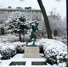 a statue of a baseball player is in the middle of snow covered bushes and trees