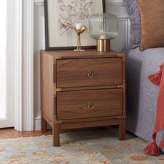 a nightstand with two drawers and a lamp on it next to a bed in a bedroom