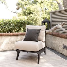 a white chair sitting on top of a wooden floor next to a brick wall and tree