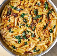 a pan filled with pasta and spinach on top of a wooden table