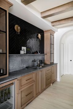 a kitchen with wooden cabinets and black marble counter tops, along with wine bottles on the shelves