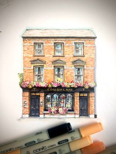 a drawing of a brick building with flowers on the window sill and two crayons next to it