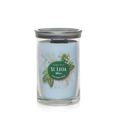 a blue candle with green leaves and white flowers on the front, in a glass jar