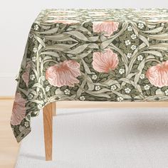 a table cloth with pink flowers and vines on green leaves, in front of a white rug