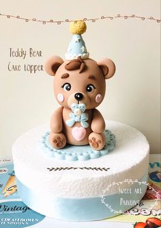 a teddy bear cake topper sitting on top of a white cake with blue icing