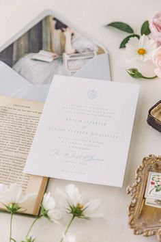 the wedding stationery is laid out on top of an open book and some flowers