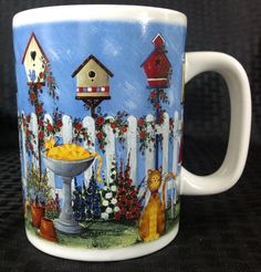 a coffee mug with a cat and bird house on it's side, in front of a fence