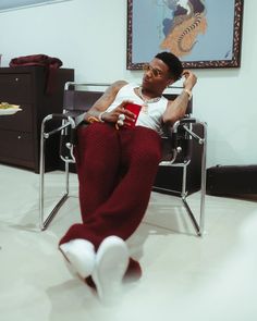 a man sitting in a chair with his feet up on the ground and wearing red pants